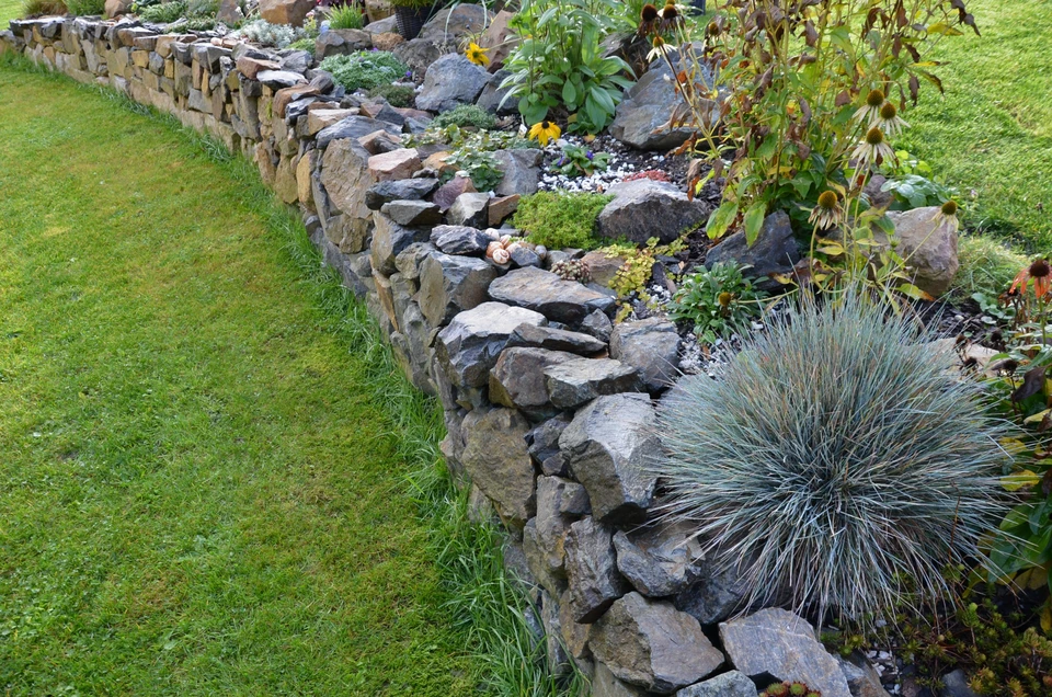 Jardin paysager extérieur avec muret en pierres naturelles délimitant une pelouse verte