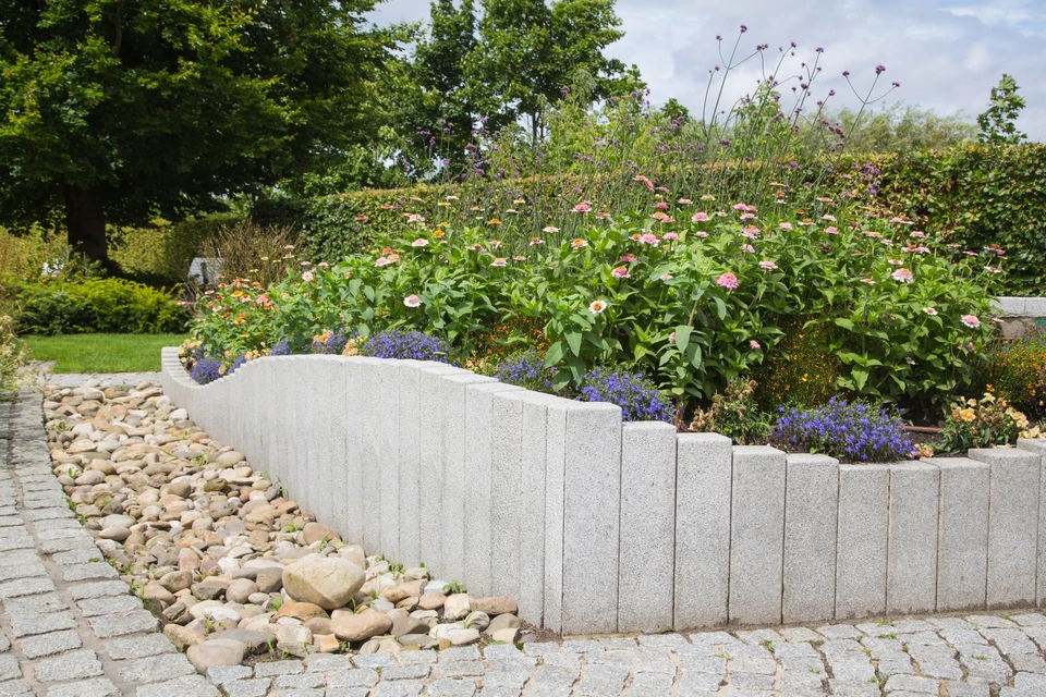 Aménagement paysager extérieur avec bordure décorative en blocs de béton texturé marron délimitant un massif végétal